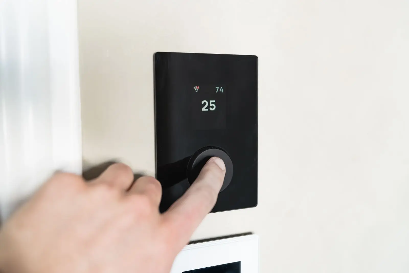 Hand adjusting a smart thermostat on a wall