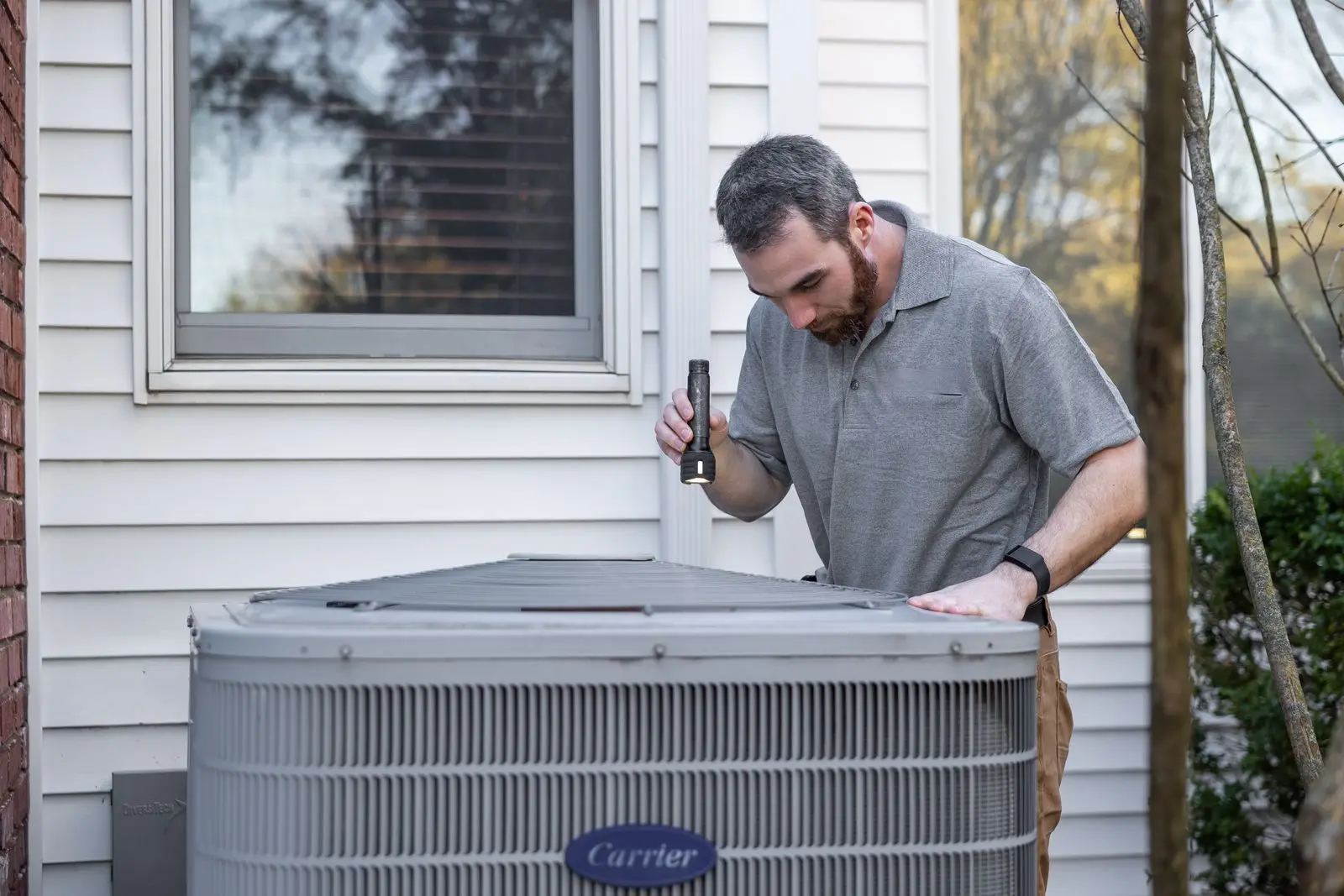 Technician inspecting an outdoor air conditioner condenser beside a house